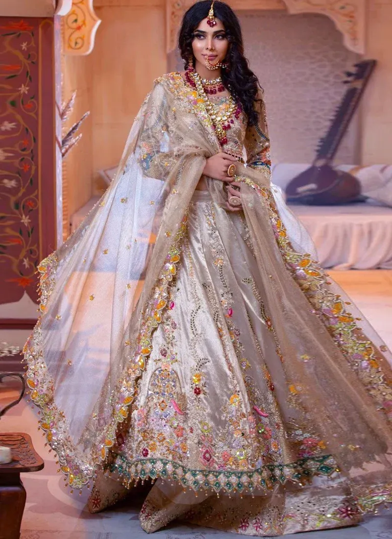 Champagne Walima Lehenga Choli with Peacock Arch Motifs Champagne Walima lehenga choli, seated front view with embroidered peacock arches and teal beaded hem.