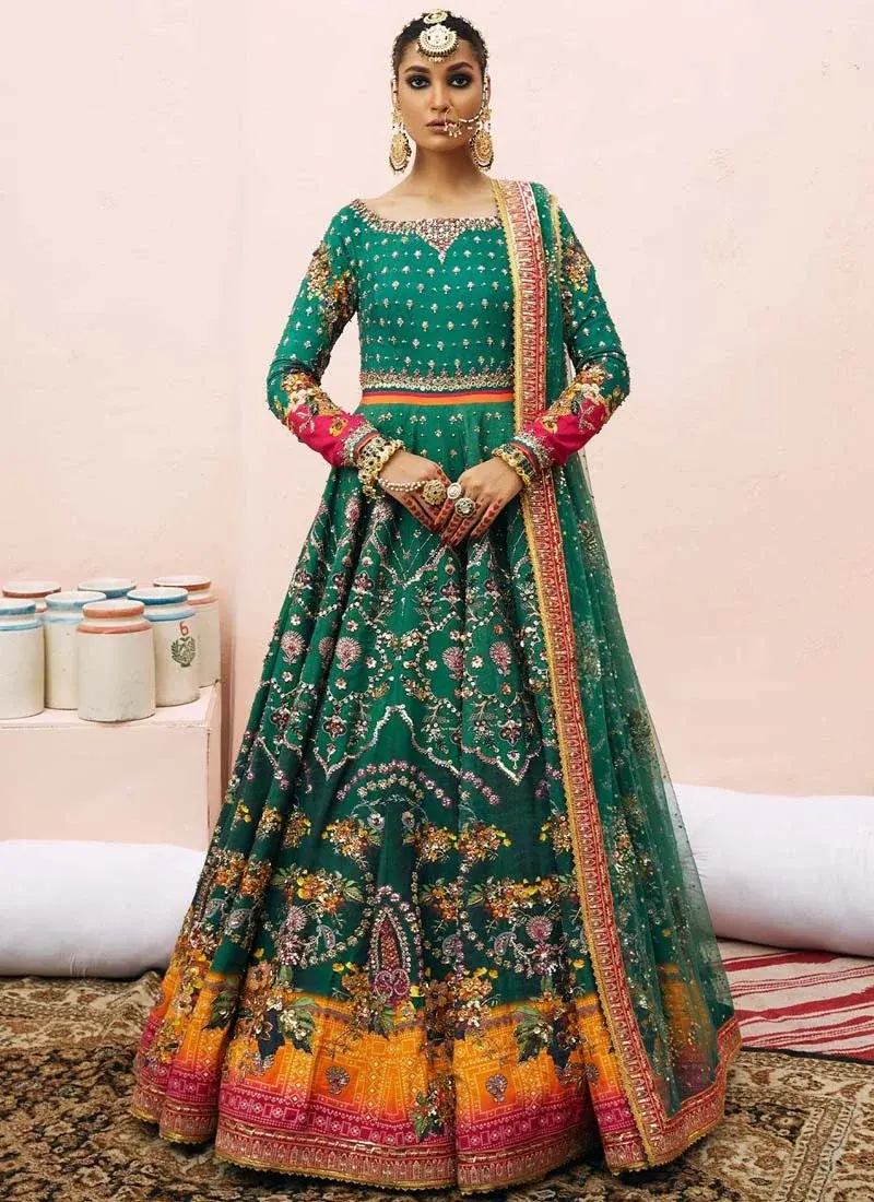 Green Mehndi Pishwas with Saffron Floral Hem Pine green Mehndi Pishwas in a seated side view with fuchsia cuffs and saffron floral hem